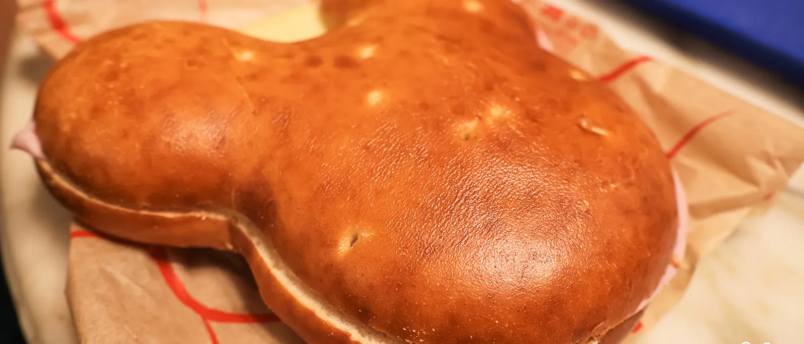 Gros pain moelleux doré en forme de tête de Mickey, garni de jambon et fromage, posé sur son sachet.