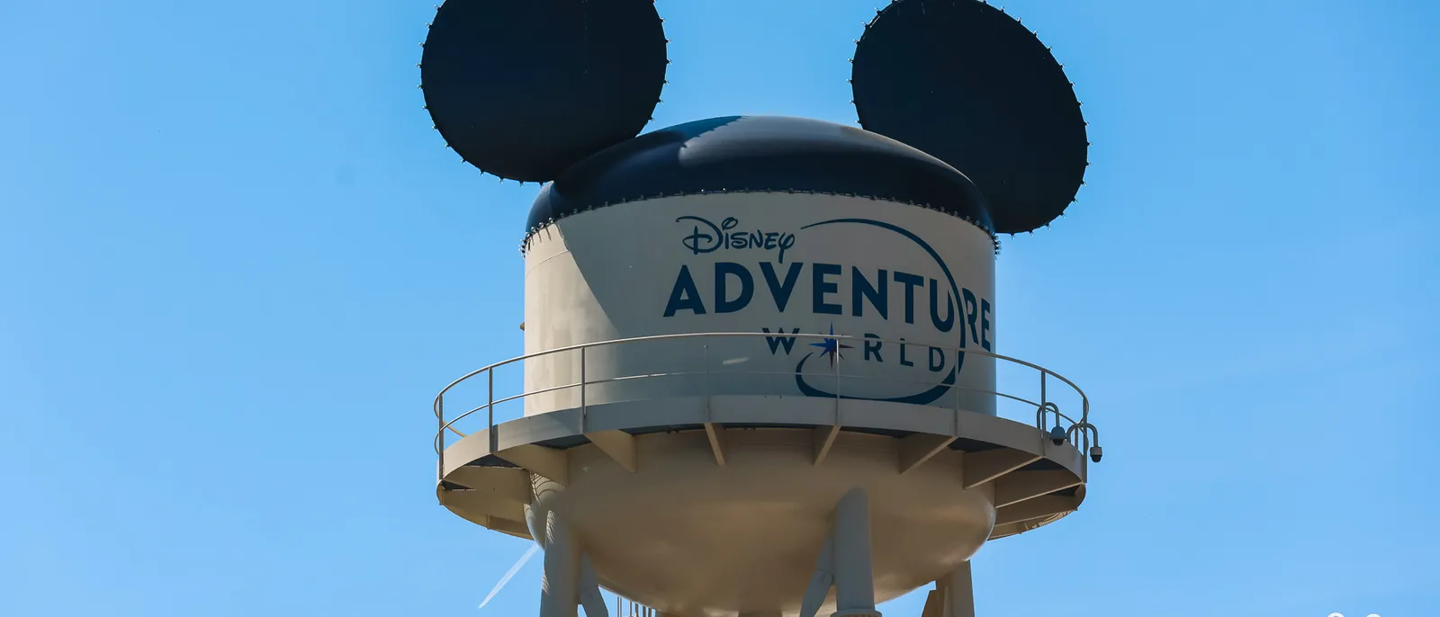 Le château d’eau coiffé d’oreilles de Mickey frappé du logo Disney Adventure World, sous un ciel bleu.