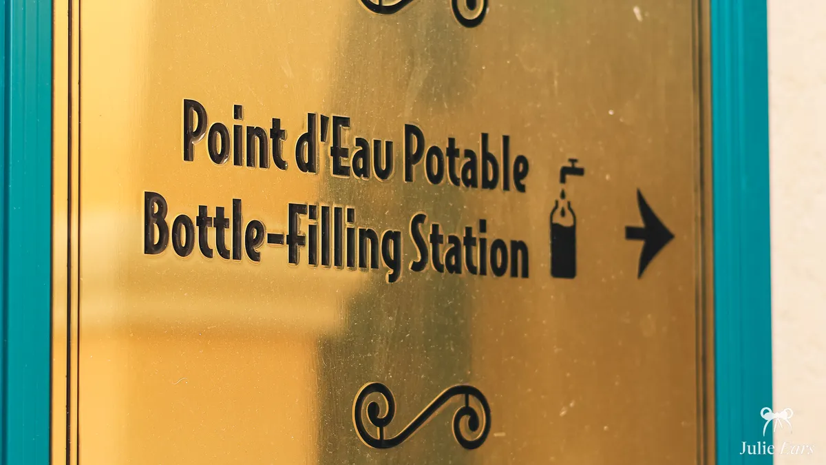 Gold, turquoise-framed sign for the drinking water bottle-filling station at Disney Adventure World, with an arrow and a tap symbol
