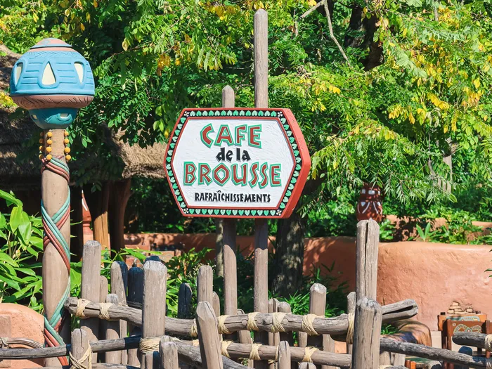 Enseigne en bois peint du Café de la Brousse au décor africain, entourée de verdure à Adventureland