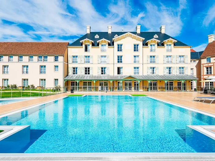 Grande piscine extérieure devant la façade du Staycity Aparthotel sous un ciel bleu