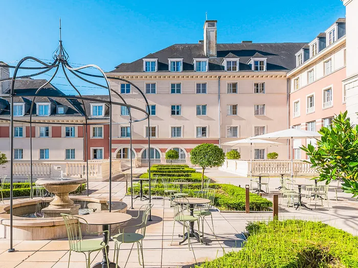 Terrasse jardin avec fontaine, tonnelle et tables devant la façade du Dream Castle Hotel