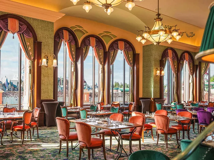 Salle Belle Époque aux fauteuils de velours et fenêtres cintrées sur le parc, restaurant The Regal View, Disneyland Paris