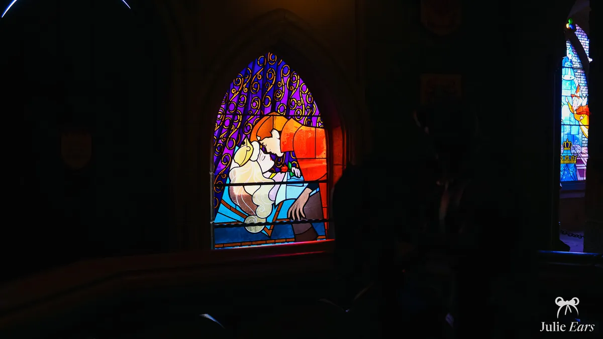 Vitrail en ogive de la Galerie de la Belle au Bois Dormant où le prince Philippe embrasse la princesse Aurore endormie, dans la pénombre du château de Disneyland Paris, avec une silhouette sombre au premier plan.