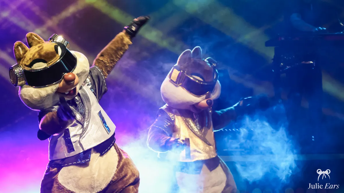 Chip ’n’ Dale dressed as DJs on stage, under colourful lights, at the Disney Music Festival at Disneyland Paris.