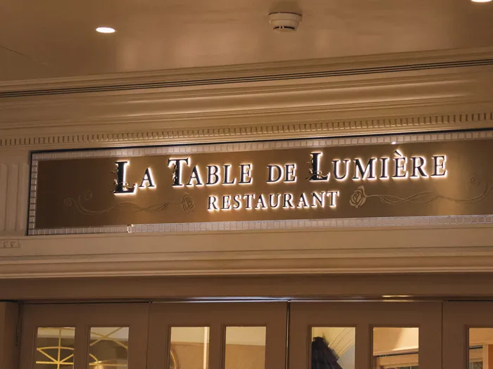 Enseigne dorée et lumineuse « La Table de Lumière Restaurant » sous des moulures élégantes, au Disneyland Hotel