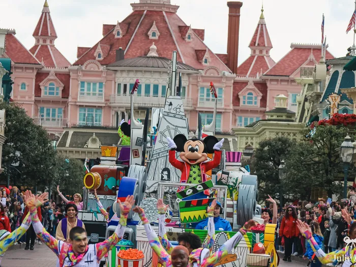 Char de Mickey et danseurs colorés de la parade A Million Splashes of Colour devant le Disneyland Hotel, Main Street