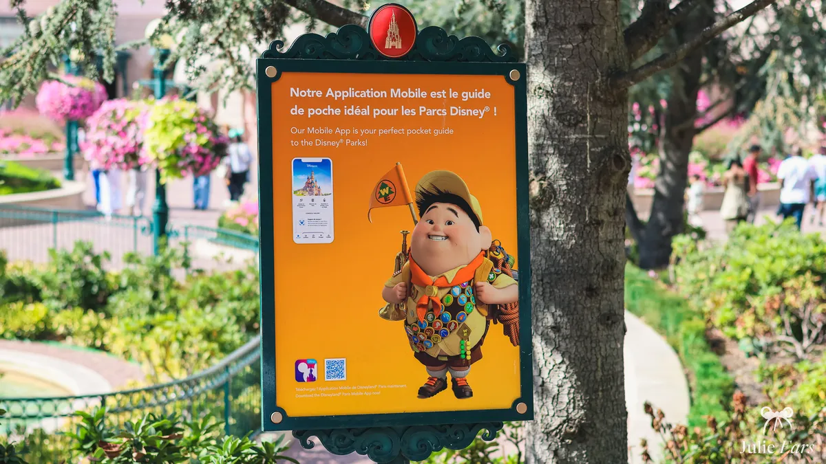 Sign in a flower bed at Disneyland Paris promoting the Disney parks mobile app, with Russell from the film Up and a QR code to download it