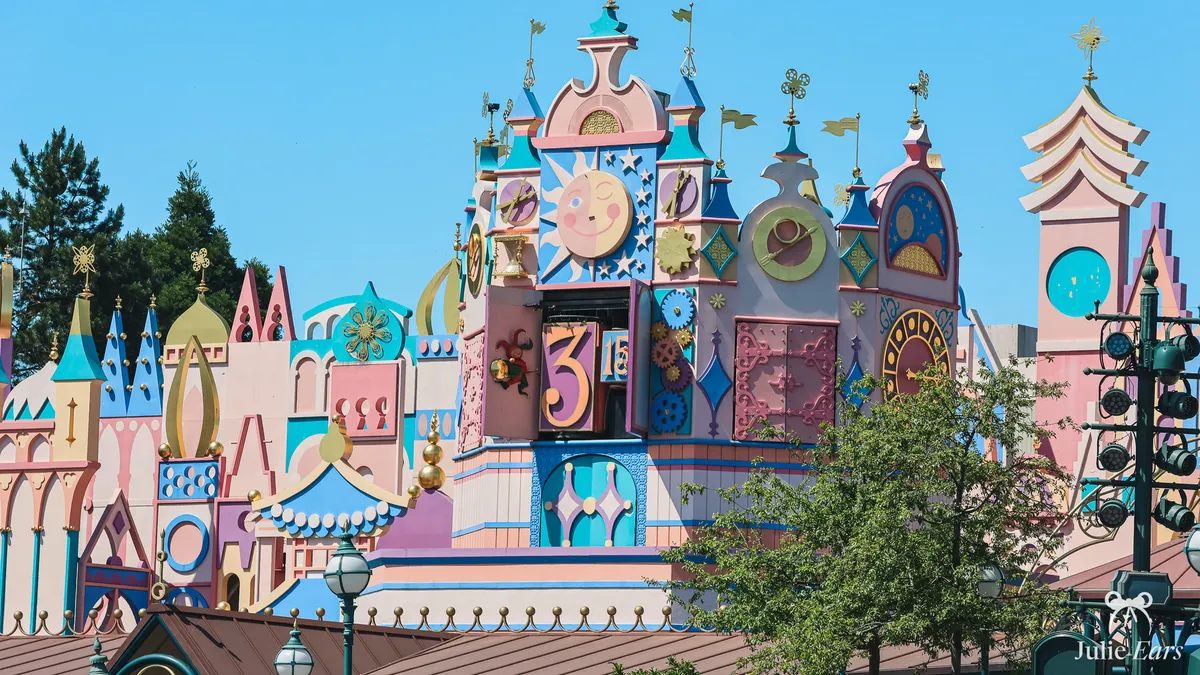 Colourful facade of "it’s a small world" in Fantasyland, with its sun-faced clock tower and pastel turrets, under a blue sky, at Disneyland Paris
