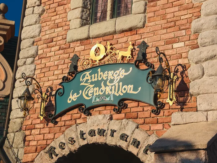 Façade en brique et enseigne verte et dorée du restaurant Auberge de Cendrillon, à Fantasyland
