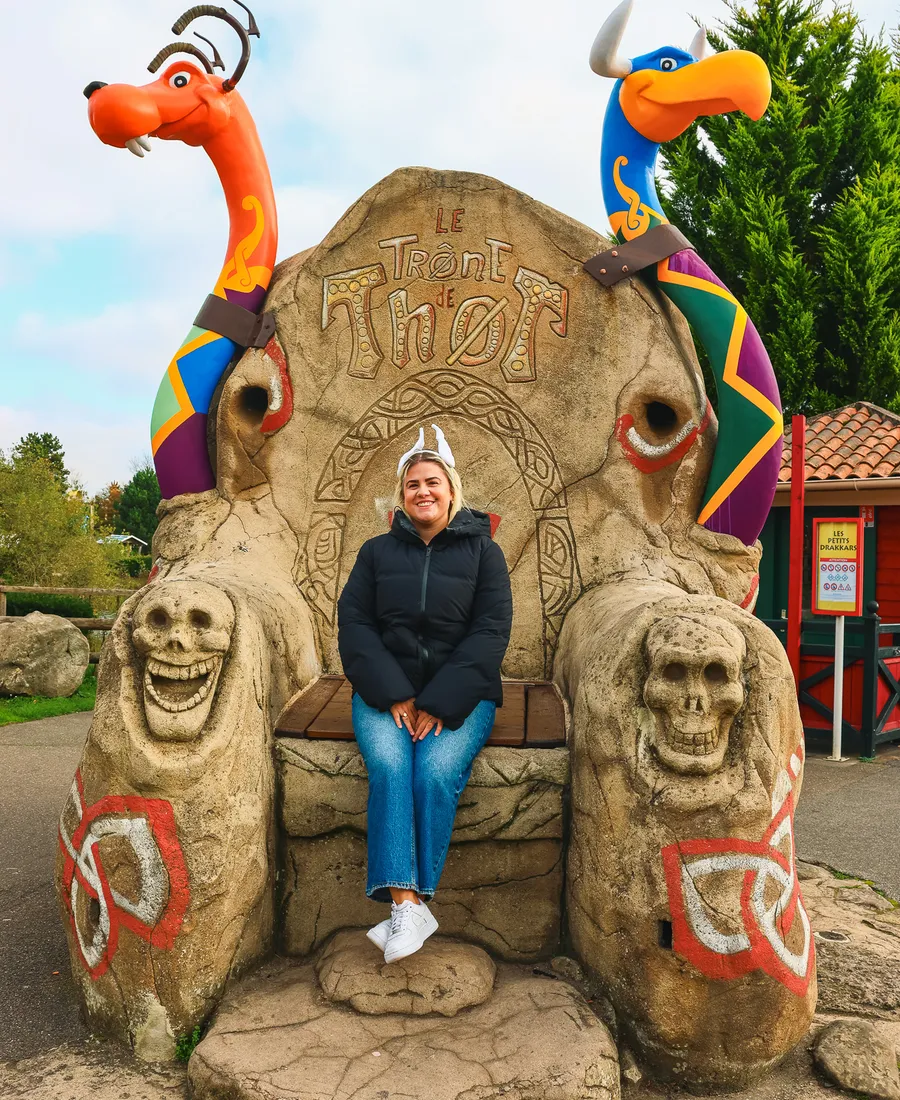Julie assise sur Le Trône de Thor, siège de pierre gravé encadré de deux dragons vikings orange et bleu
