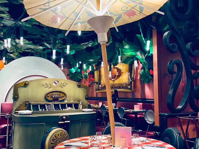 Table à nappe vichy rouge dressée sous une ombrelle en papier, décor surdimensionné du Bistrot Chez Rémy