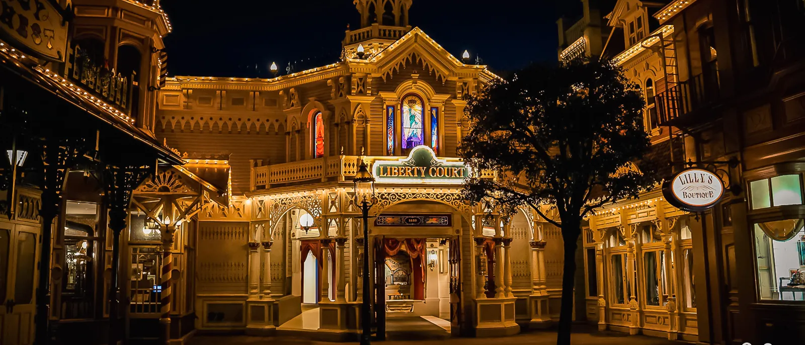 Le passage Liberty Court illuminé de guirlandes la nuit sur Main Street USA, avec la boutique Lilly’s à droite.