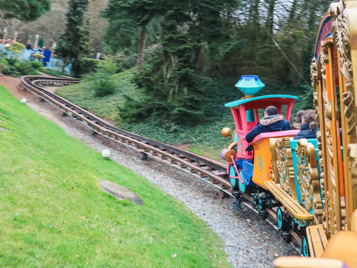 Wagons colorés du petit train Casey Jr avec des visiteurs, longeant une voie en pente au milieu de la verdure à Fantasyland