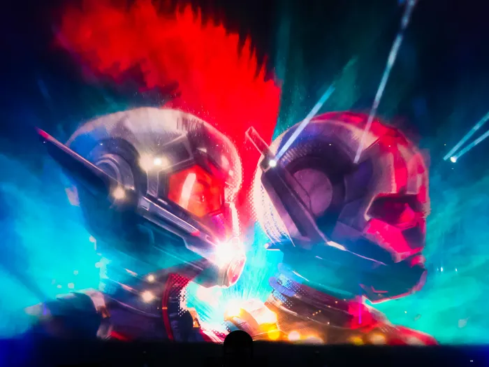 Deux casques d’Ant-Man face à face projetés sur un écran d’eau en bleu et rouge, spectacle nocturne.