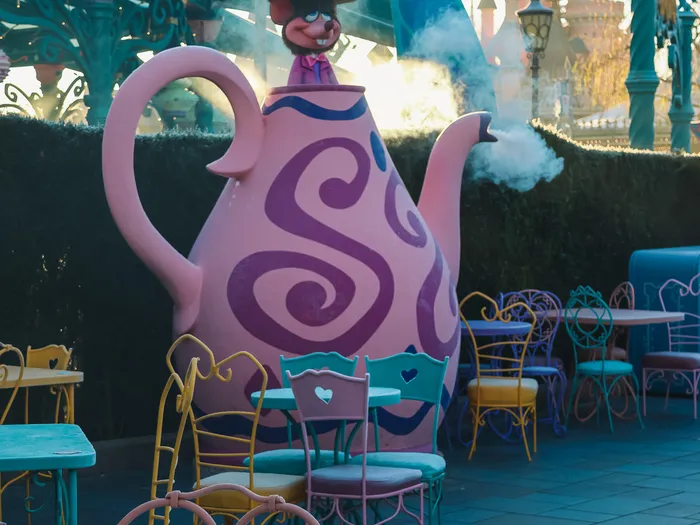 Giant pink March Hare Refreshments teapot letting off steam, with the Dormouse under the lid, the colourful tables and the castle in the background
