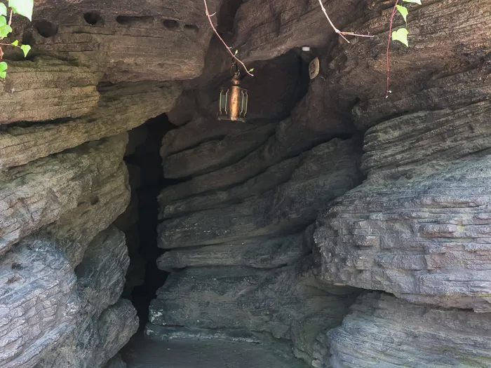 Entrée d’une grotte creusée dans la roche, éclairée d’une lanterne et bordée de lierre, à Adventure Isle