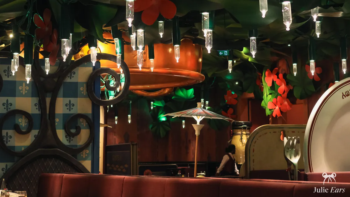 Bistrot Chez Rémy dining room, Disneyland Paris: giant fairy lights, cocktail umbrella, copper pan, giant plate and cutlery behind red banquettes