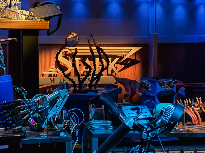 Établi encombré de robots et outils devant l’enseigne Spider-Bot, décor de la file de Spider-Man W.E.B. Adventure.