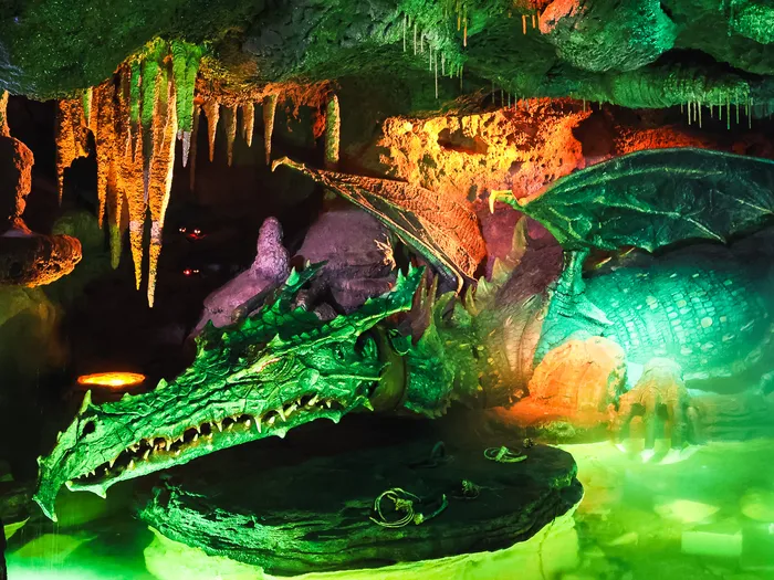 Dragon animatronique aux mâchoires ouvertes, éclairé de vert et d’orange dans la grotte de La Tanière du Dragon.