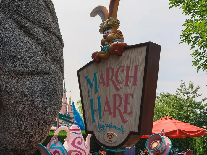 Enseigne en bois du March Hare Refreshments coiffée du Lièvre de Mars, théières colorées au premier plan à Fantasyland