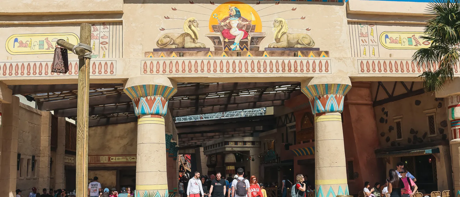 Façade égyptienne aux colonnes peintes turquoise et rouge, fresque de Cléopâtre entre deux sphinx, visiteurs sous le porche