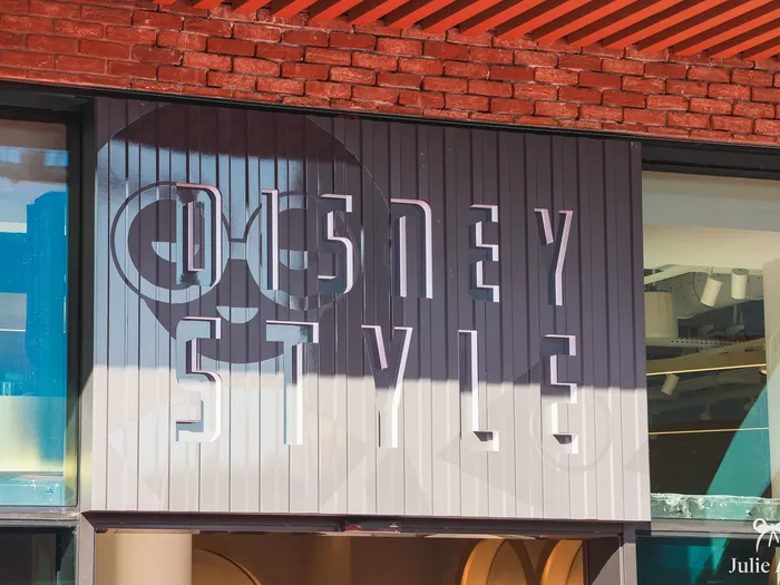 Enseigne grise Disney Style avec tête de Mickey, sous une façade de briques rouges