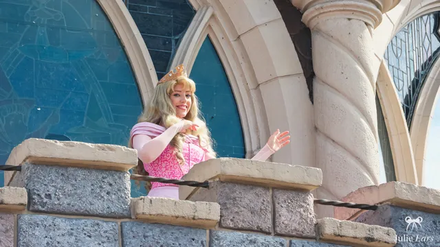 La princesse Aurore, robe rose et couronne dorée, salue depuis un balcon du château à Disneyland Paris.
