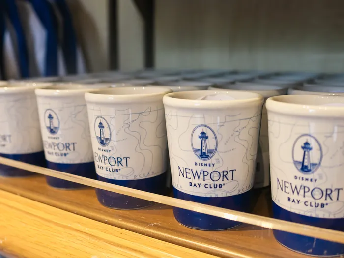 Row of white and blue mugs with the Disney Newport Bay Club logo and a nautical chart pattern.