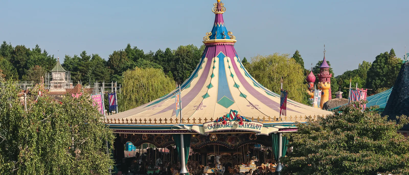 Le Carrousel de Lancelot avec sa toiture violette et crème, entouré d’arbres, à Fantasyland, Disneyland Paris.