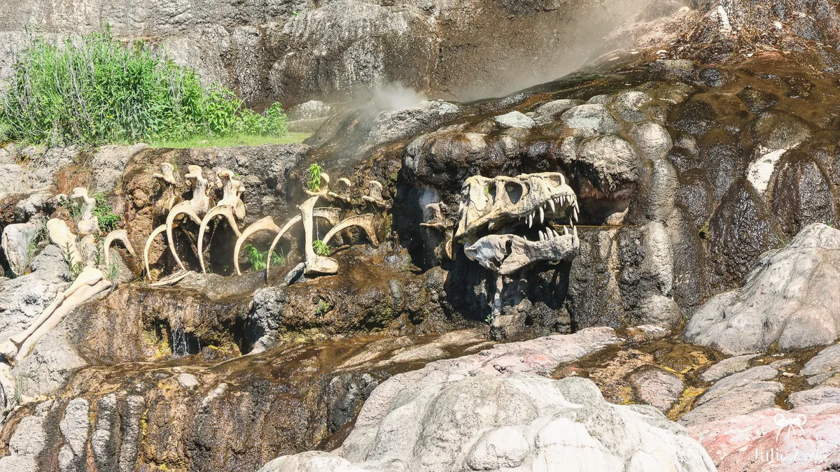 Dinosaur skeleton set in the rock by the Rivers of the Far West, jaws open and ribs lined up, under wisps of steam, Frontierland, Disneyland Park
