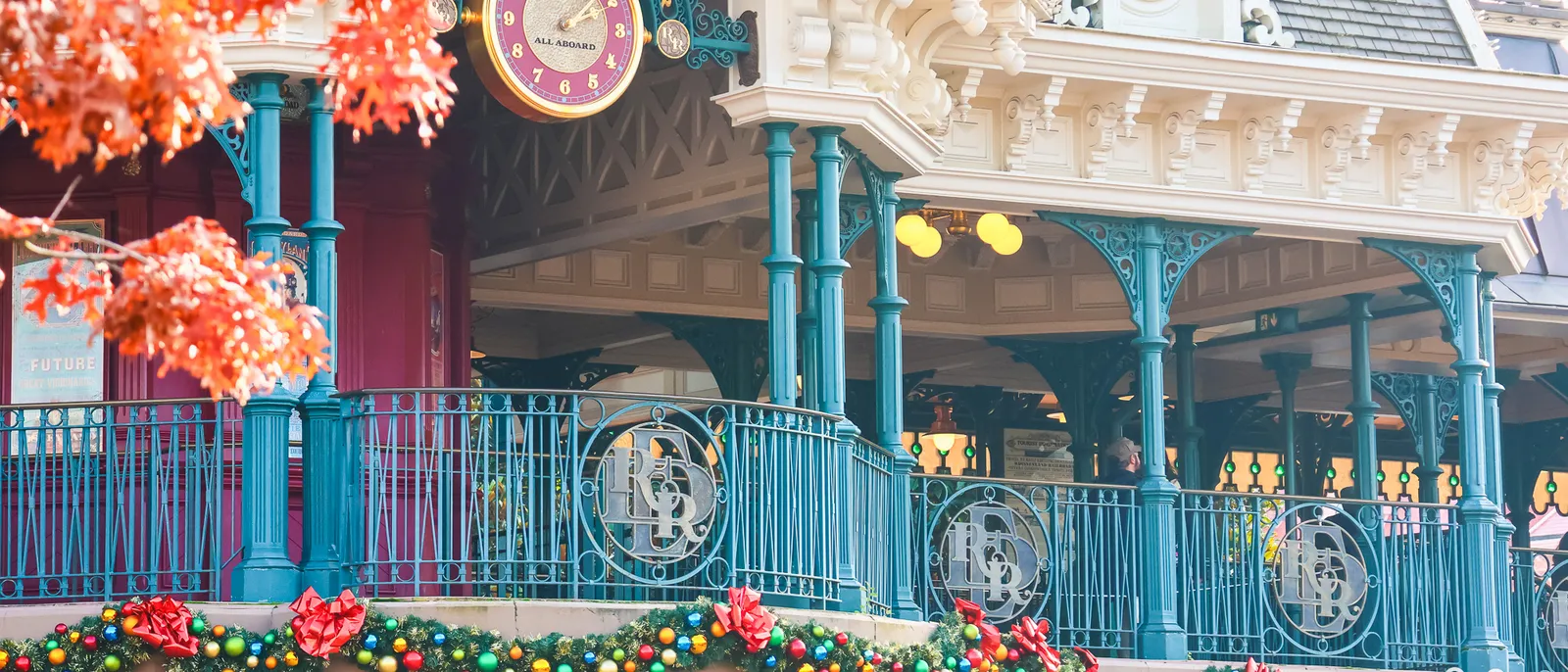 Horloge et balustrade turquoise de la gare Main Street ornées d’une guirlande de Noël avec boules colorées et nœuds rouges.