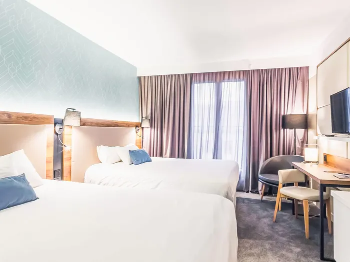 Chambre de l’hôtel Elysee Val d’Europe avec deux lits, tête de lit turquoise géométrique et bureau.