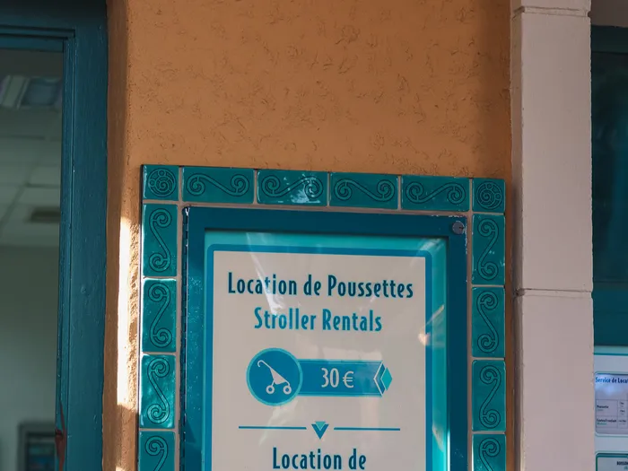 Price board framed with turquoise tiles showing pushchair hire at €30 and wheelchair hire at €25 at Disneyland Paris.
