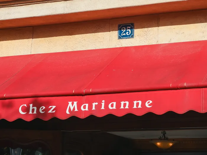 Red awning of the Chez Marianne shop, its name in white letters and a blue number 25 street plaque on the pale stone front, Disneyland Paris