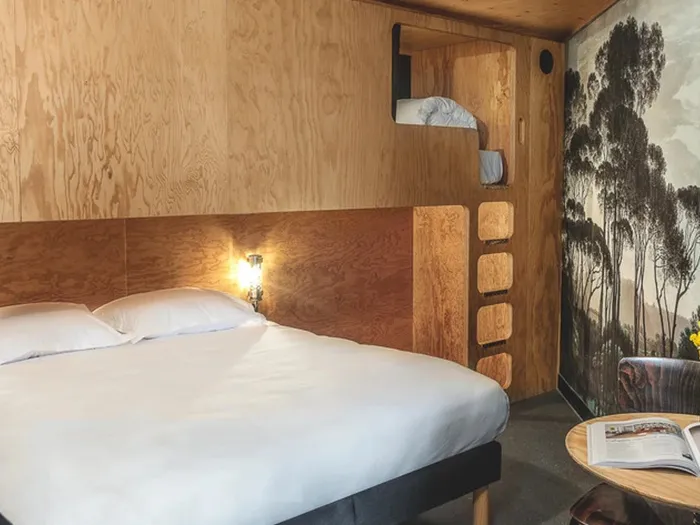 Room at the Eklo hotel with a double bed and a raised single bed, a light wood wall and tree-patterned wallpaper.