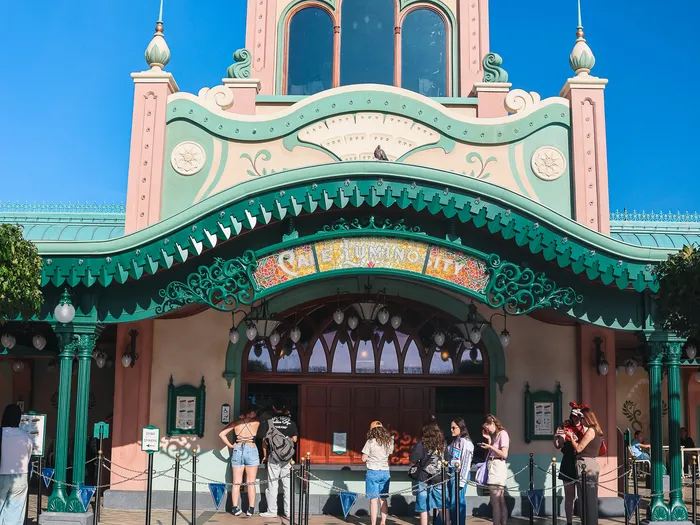 Facade of Café Luminosity at Disneyland Paris, turquoise dome and pale pink walls, with visitors waiting in front of the counters