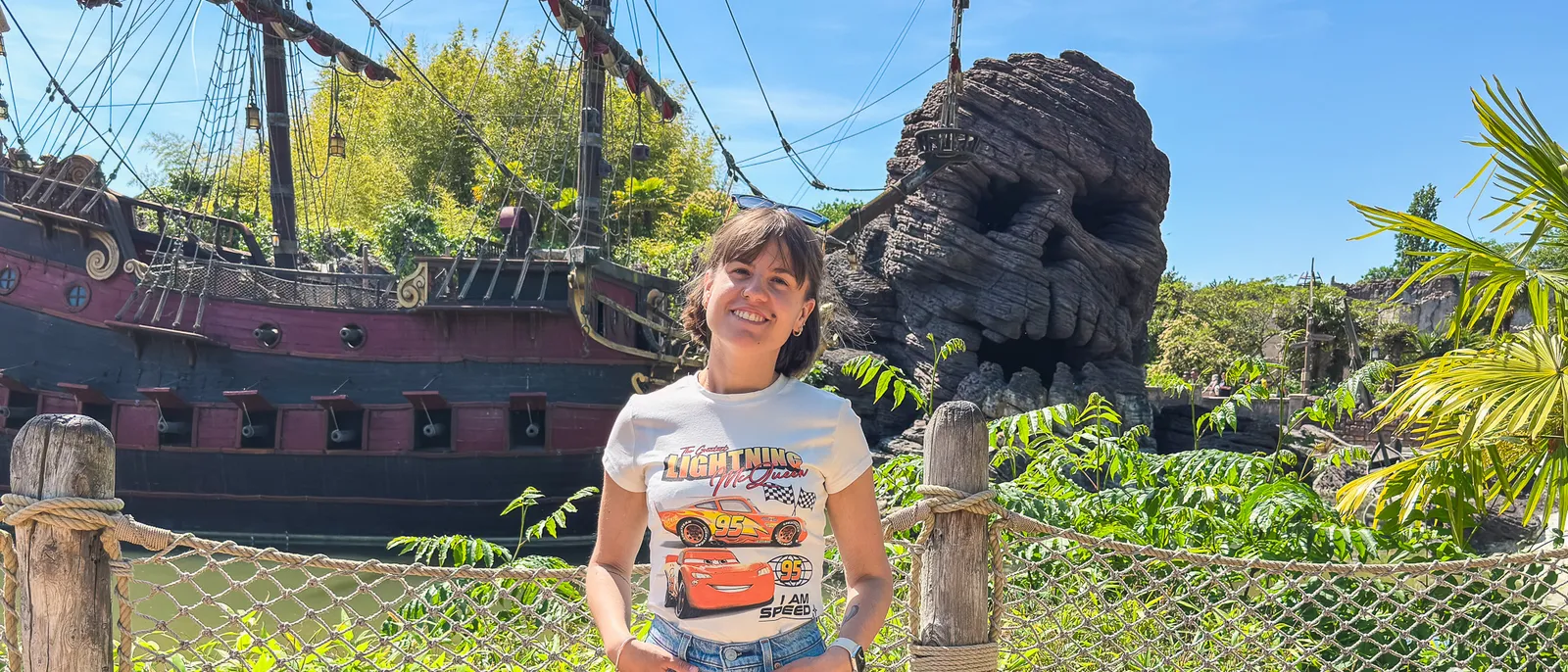 Femme souriante posant devant le galion pirate et le rocher crâne d’Adventureland