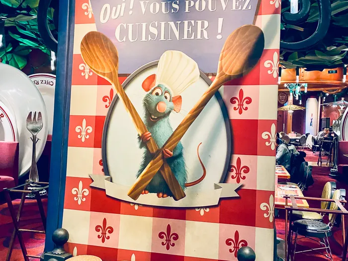 Grand panneau Chef Rémy « Oui, vous pouvez cuisiner » avec cuillères géantes et tabourets bouchons dans la salle du restaurant