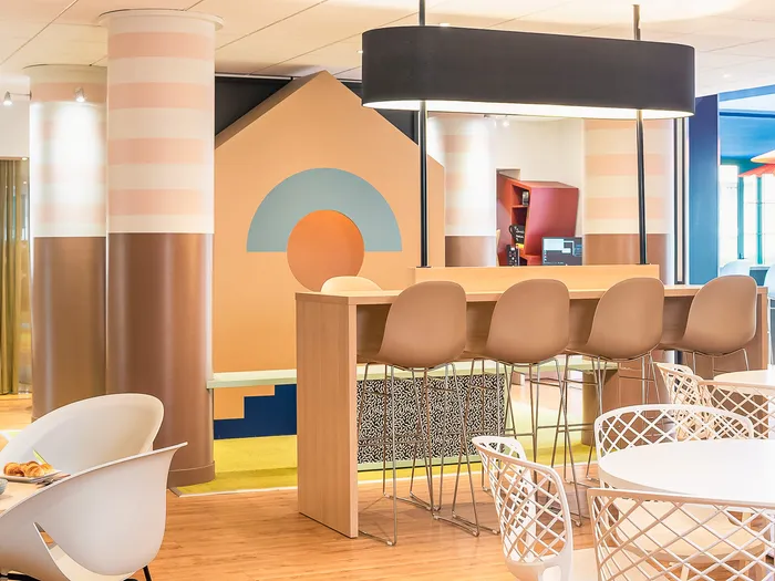 Espace petit-déjeuner de l’Adagio Aparthotel avec bar haut, tables rondes et décor coloré