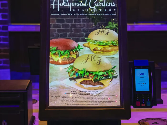 Borne de commande tactile du restaurant The Hollywood Gardens affichant trois burgers signés HG et un terminal de paiement.