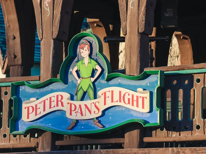 Enseigne en bois de Peter Pan’s Flight avec le personnage debout, façade à colombages de Fantasyland.