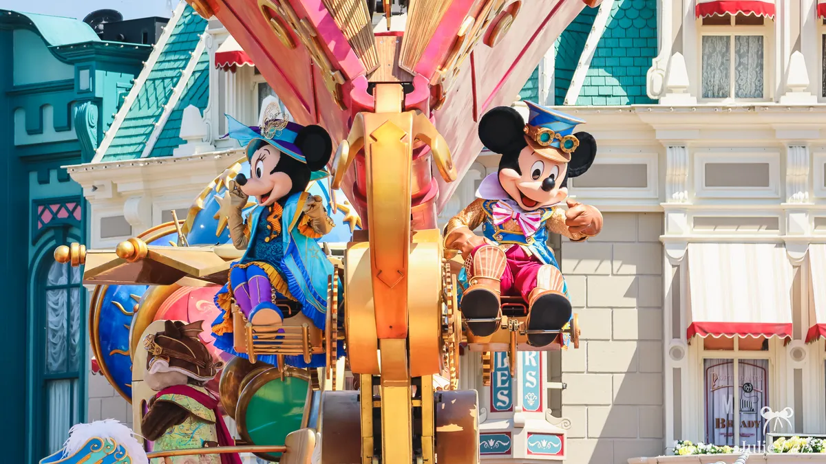 Mickey and Minnie in blue and gold steampunk-inspired costumes on a Disney Stars on Parade float, in front of the facades of Main Street U.S.A. at Disneyland Paris