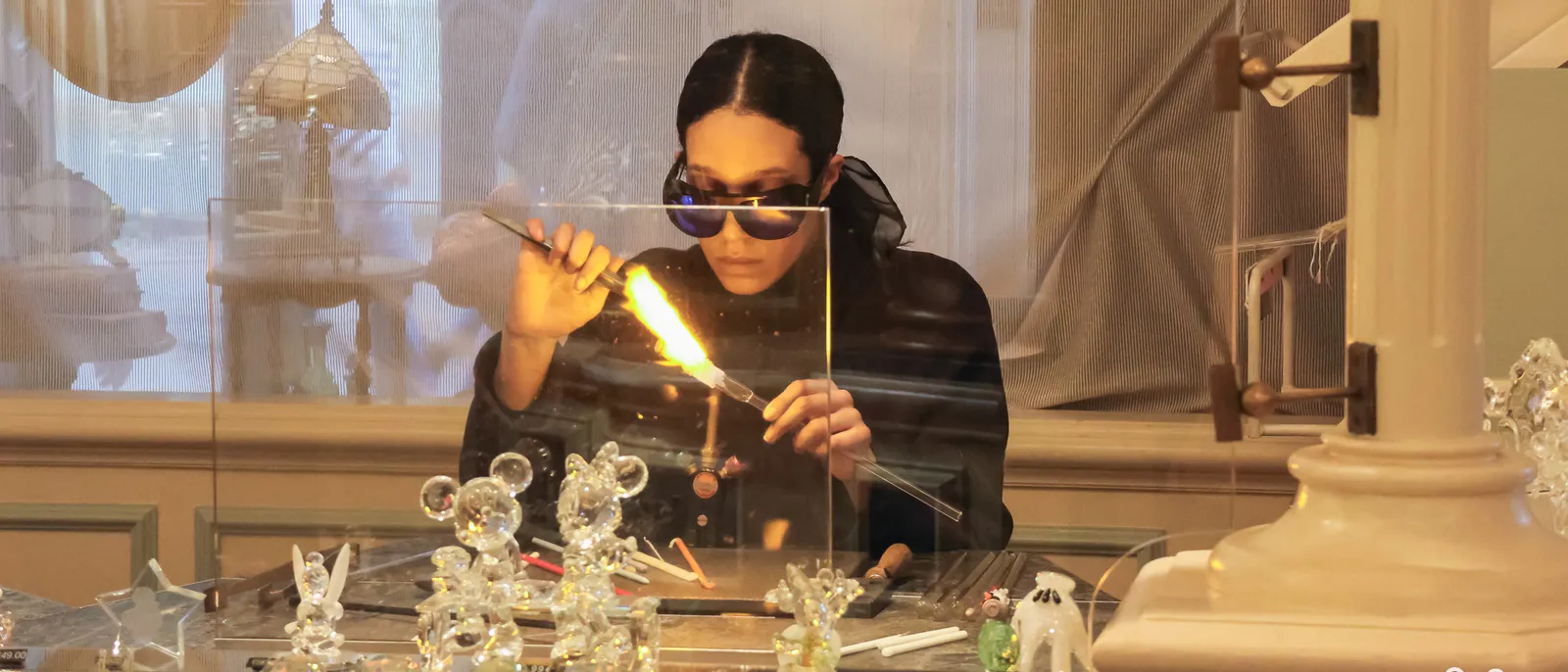 Artisan verrier Arribas façonnant une figurine de verre au chalumeau, petits Mickey en cristal alignés sur le comptoir.