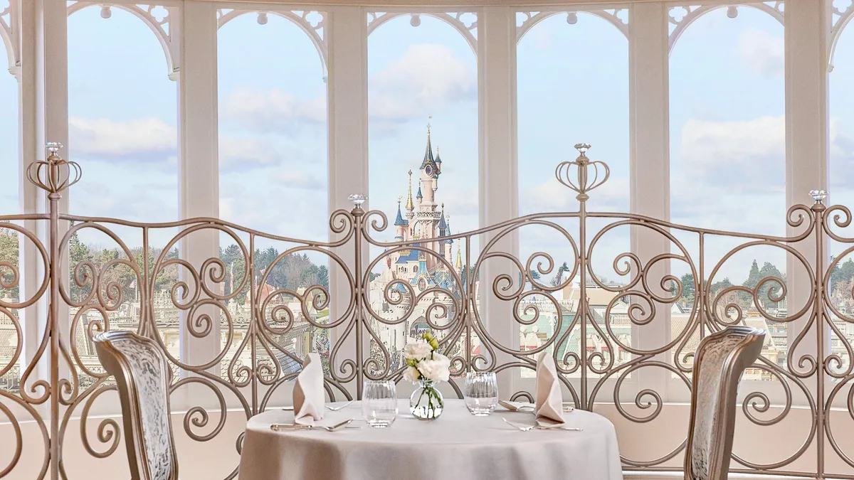 Table dressée devant une baie vitrée du Disneyland Hotel avec vue sur le Château de la Belle au Bois Dormant
