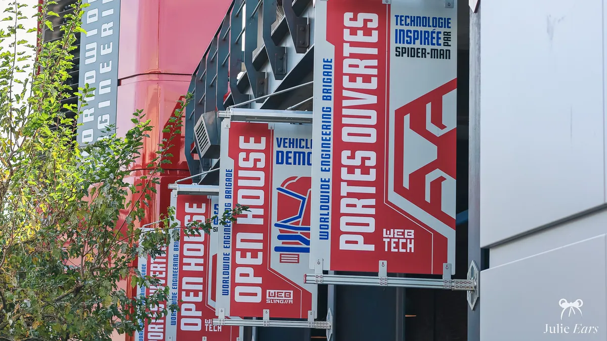 Red and white Worldwide Engineering Brigade banners reading "Portes ouvertes" and "Open House" on the Spider-Man W.E.B. Adventure building at Avengers Campus