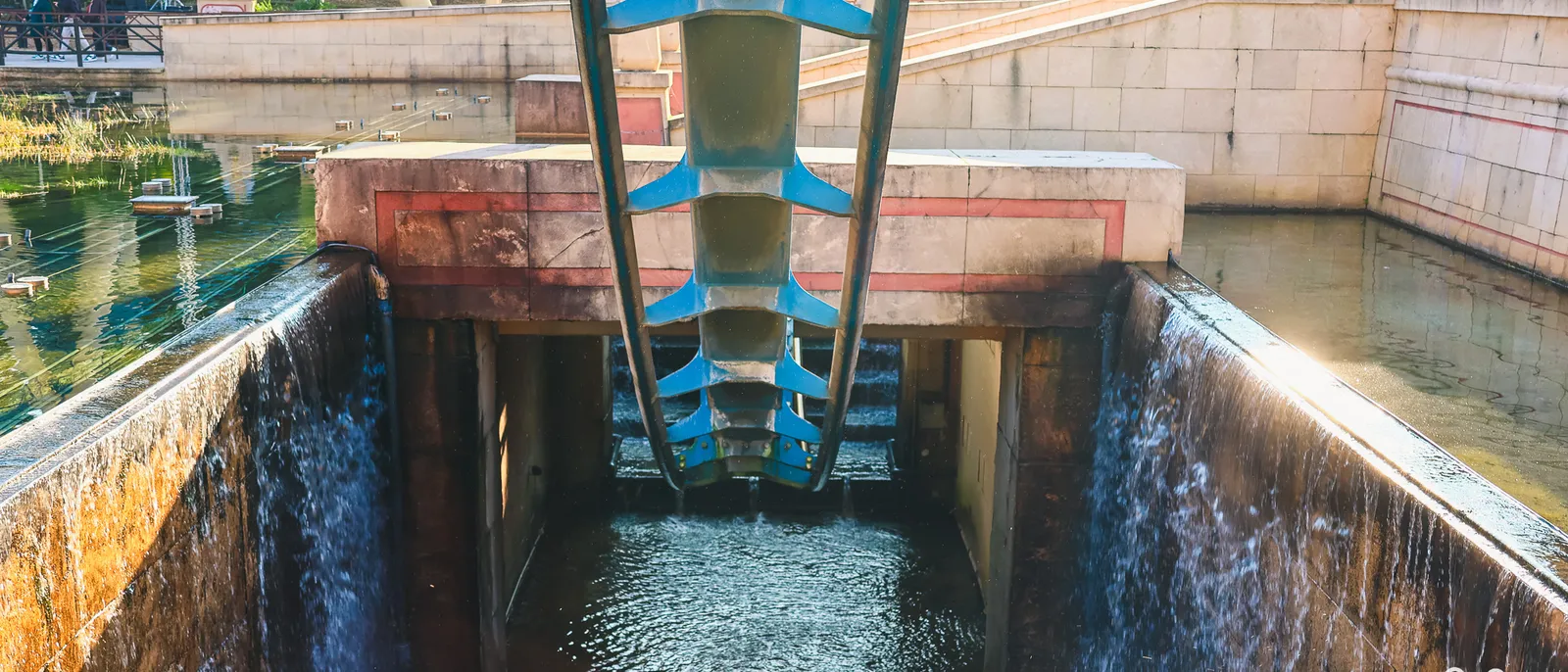 Rails bleus d’OzIris plongeant vers un bassin, murs de pierre égyptiens et rideaux d’eau ruisselant de chaque côté
