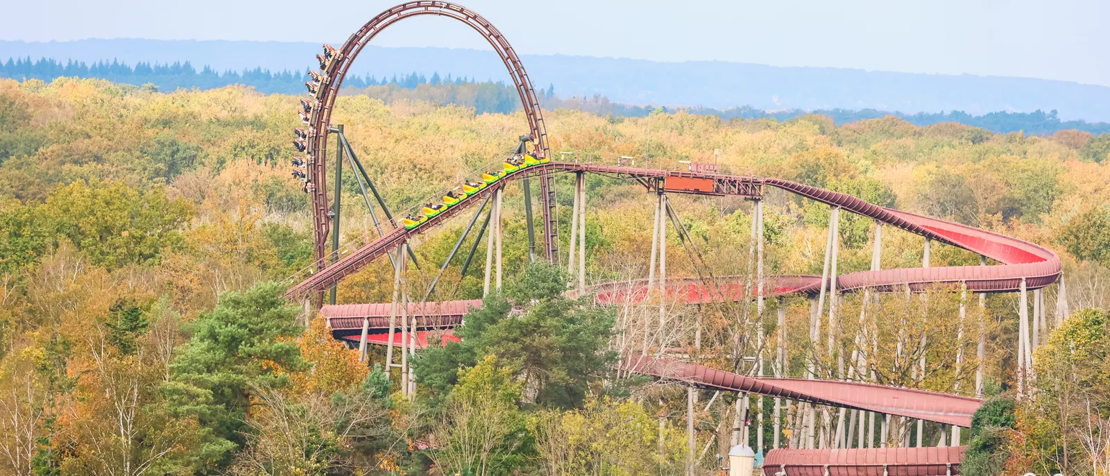 Piste rouge de La Trace du Hourra serpentant dans la forêt aux couleurs d’automne, grand looping en arrière-plan