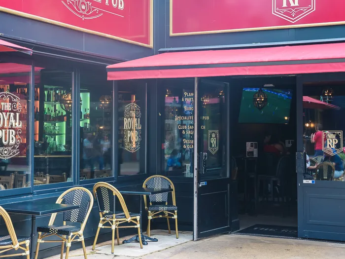 Terrasse extérieure du Royal Pub au Disney Village, tables et chaises en rotin devant les baies vitrées éclairées.