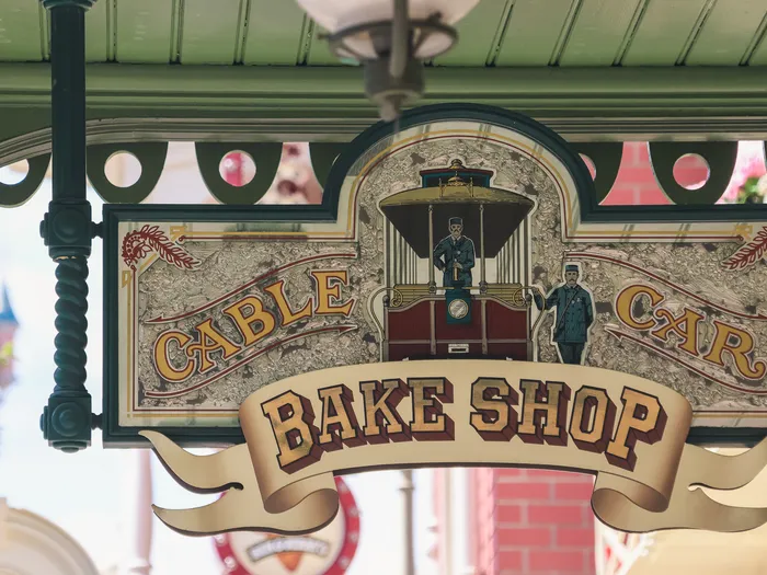 L'enseigne ouvragée du Cable Car Bake Shop, ornée d'un tramway, sous l'auvent vert de Main Street USA.